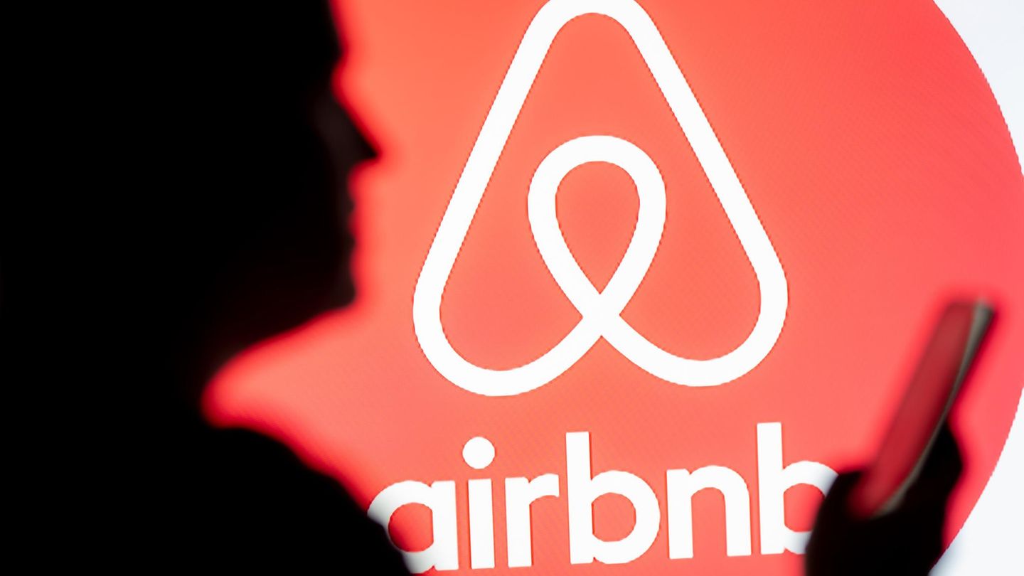 Eine Frau schaut auf ihr Smartphone, im Hintergrund ist das Airbnb-Logo zu sehen