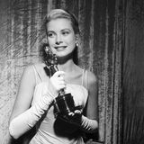 Grace Kelly 1955 mit dem Oscar in der Hand. Sie trägt eine weiße Robe mit Spaghettiträgern