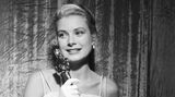 Grace Kelly 1955 mit dem Oscar in der Hand. Sie trägt eine weiße Robe mit Spaghettiträgern