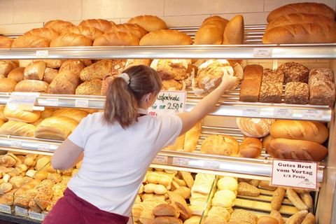 Eine Bäckerin holt ein Brot aus der Auslage hinter der Theke