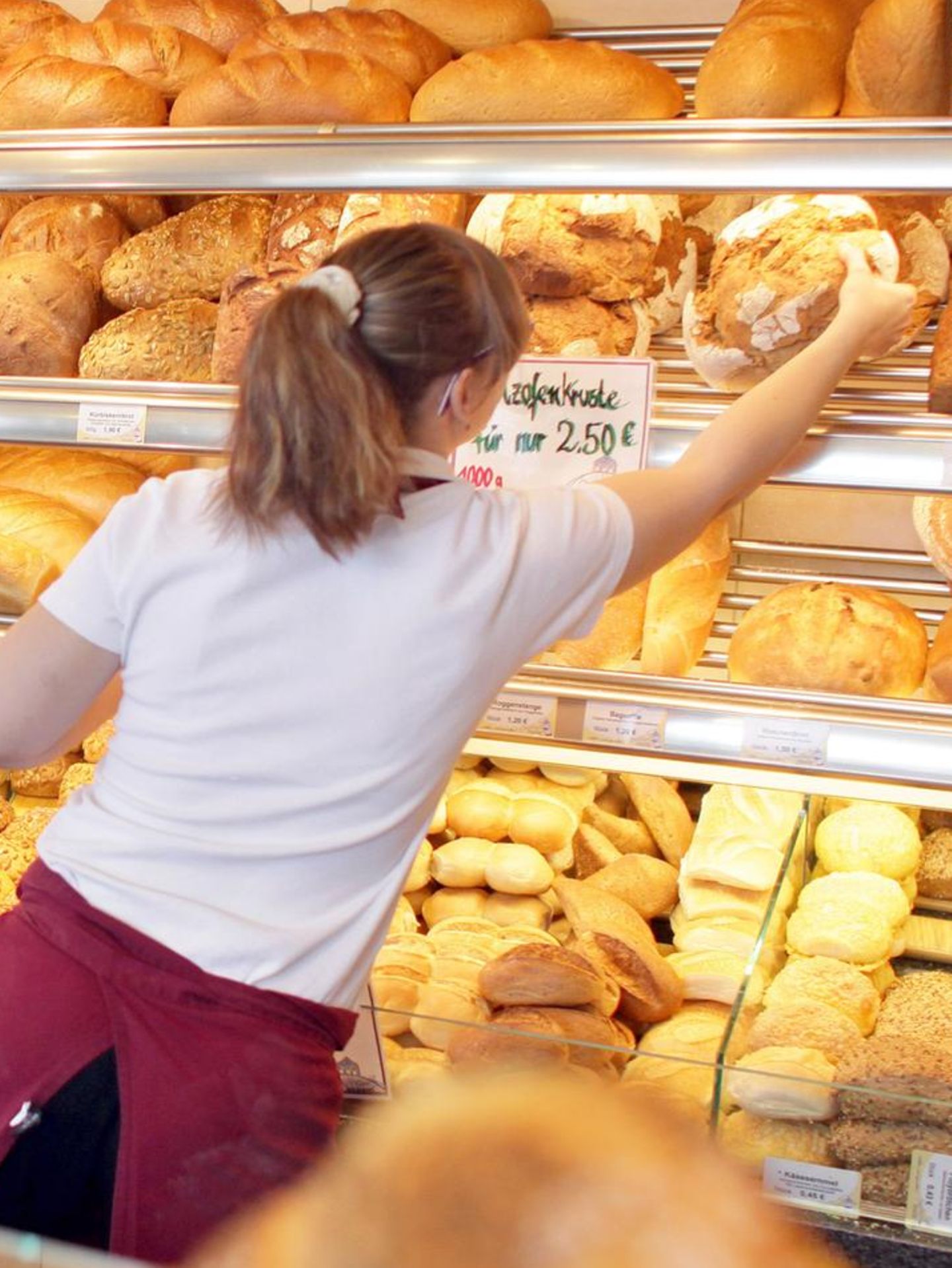 Eine Bäckerin holt ein Brot aus der Auslage hinter der Theke