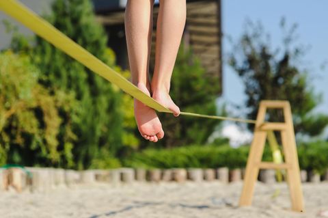 Slackline ohne Baum: Frau läuft am Strand über eine Slackline