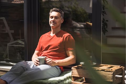 Ein Mann sitzt in der Sonne mit geschlossenen Augen und einer Tasse in der Hand