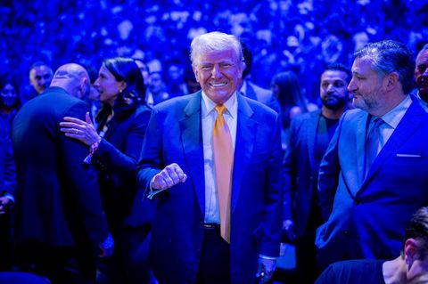 Donald Trump lächelt und steht in einer Menschenmenge, der Raum ist blau beleuchtet