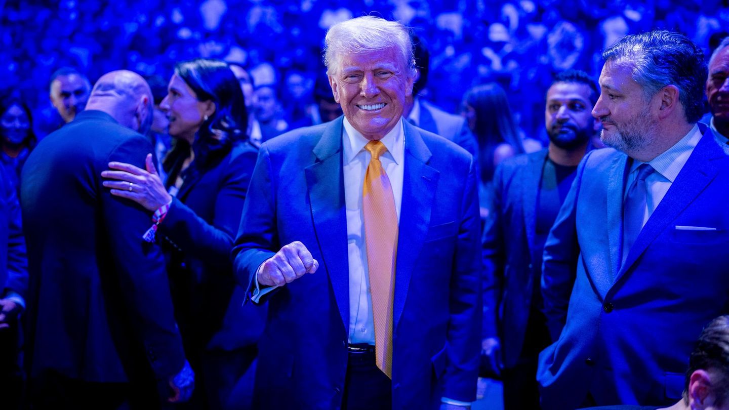 Donald Trump lächelt und steht in einer Menschenmenge, der Raum ist blau beleuchtet