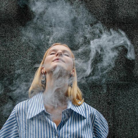 A woman with blond hair puts her head back, around her is a cigarette smoke