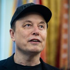 Elon Musk steht mit schwarzem Cap auf dem Kopf im Oval Office im Weißen Haus