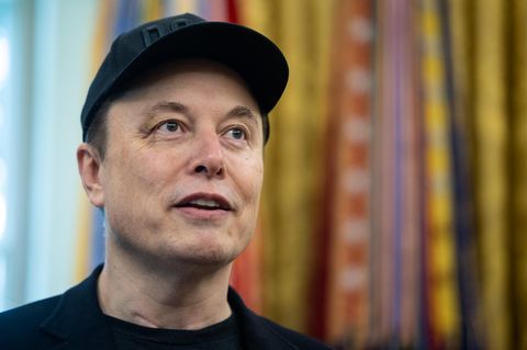 Elon Musk steht mit schwarzem Cap auf dem Kopf im Oval Office im Weißen Haus