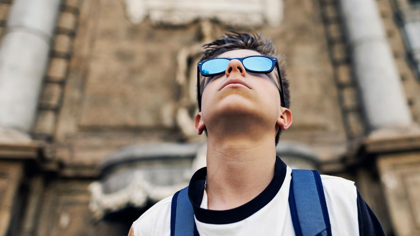 Junger Mann guckt mit verspiegelter Sonnenbrille in den Himmel