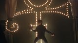 Prince im Dunkel der Bühne vor einem leuchtenden Symbol