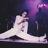 Prince im weißen Anzug macht bei einem Auftritt Spagat auf der Bühne