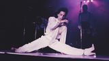 Prince im weißen Anzug macht bei einem Auftritt Spagat auf der Bühne