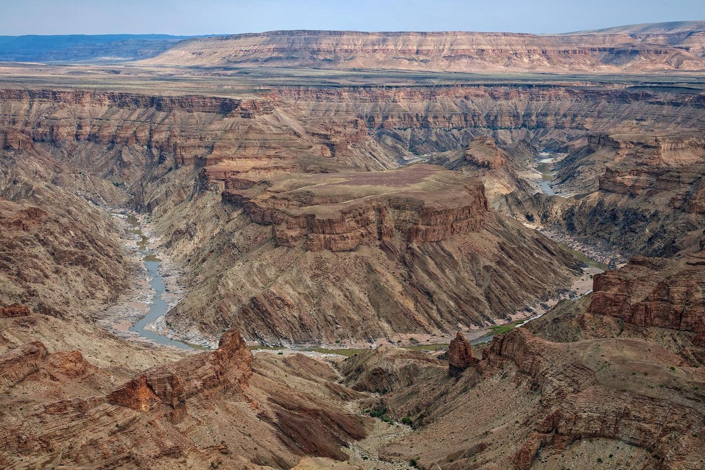 Fish River Canyon, Namibia Der Süden Namibias ist trocken. In der kargen und zerklüfteten Landschaft überleben nur Pflanzen und Tiere, die in der Lage sind, sich diesen Gegebenheiten anzupassen. Doch es gibt eine Lebensader, die diese Region mit Leben füllt: der Fish River. Der Fluss fräst sich seit der Pluvialzeit vor 550 Millionen Jahren seinen Weg durch die staubige Erdkruste und hat so den zweitgrößten Canyon der Welt geformt. Die Furche des Fish River Canyons ist insgesamt 160 Kilometer lang, bis zu 550 Meter tief und in Teilen bis zu 27 Kilometer breit. Nur in ein paar Wochen im Jahr lässt die Naturschutzbehörde auch Wanderer in die Schlucht hinabsteigen, die aufgrund von Temperaturen bis zu 50 Grad und Springfluten als sehr tückisch gilt