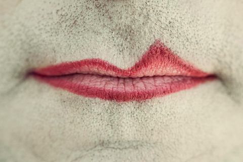 Der Mund eines Mannes, umgeben von Bartstoppeln, ungleich mit rotem Lippenstift geschminkt