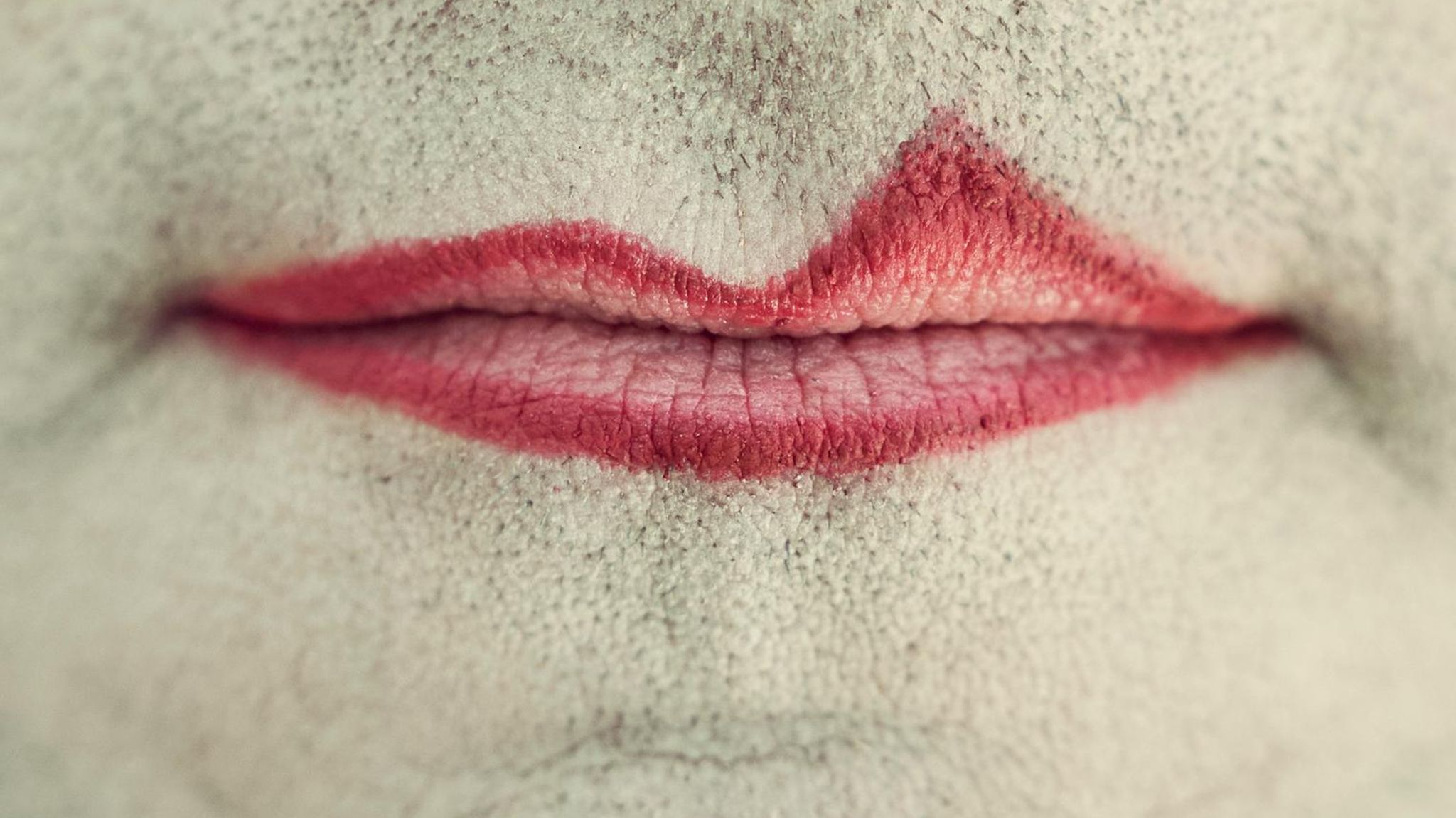 Der Mund eines Mannes, umgeben von Bartstoppeln, ungleich mit rotem Lippenstift geschminkt