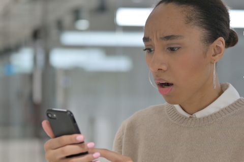 Eine Frau schaut erschrocken auf ihr smartphone. Oben rechts ist das Whatsapp-Logo zu sehen