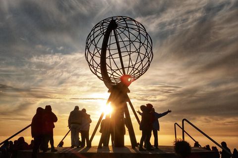 Die Silhouetten von Touristen und die einer Statue zeichnen sich gegen den Abendhimmel am Nordkap in Norwegen ab