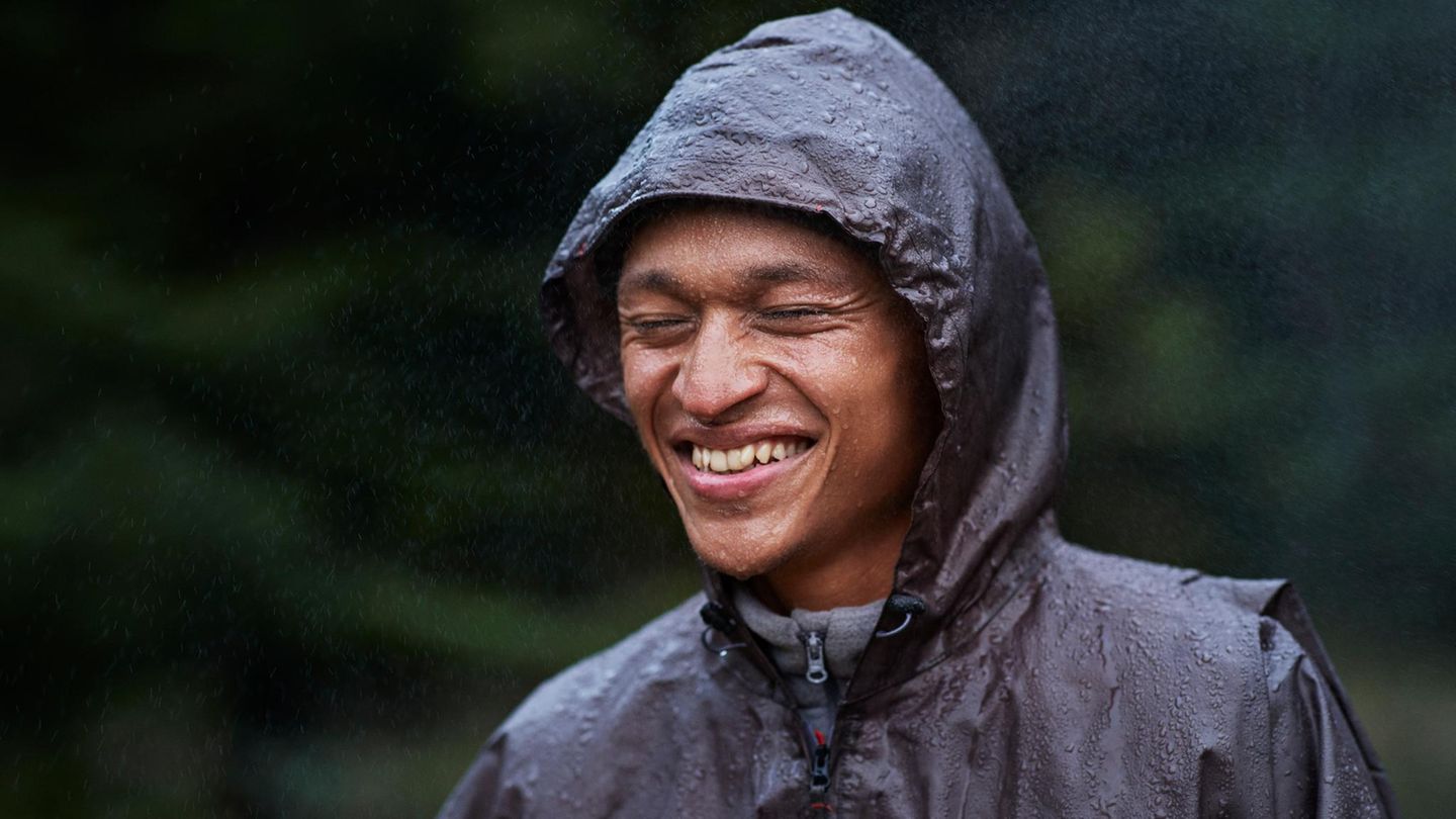 Ein Mann steht mit seiner Regenjacke im Regen