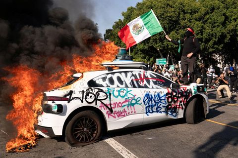 Szenen aus Los Angeles: Ein vermummter Demonstrant steht mit Mexiko-Flagge auf der Motorhaube eines brennenden Autos, auf das "Fuck ICE" geschmiert wurde. ICE ist die Einwanderungsbehörde der USA, die großflächig im Land auf Anweisung Trumps Razzien gegen illegale Einwanderer durchführt