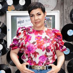 Reyhan Şahin aka Lady Bitch Ray blickt in die Kamera. Sie hat kurze, dunkle Haare und trägt eine pink geblümte Bluse