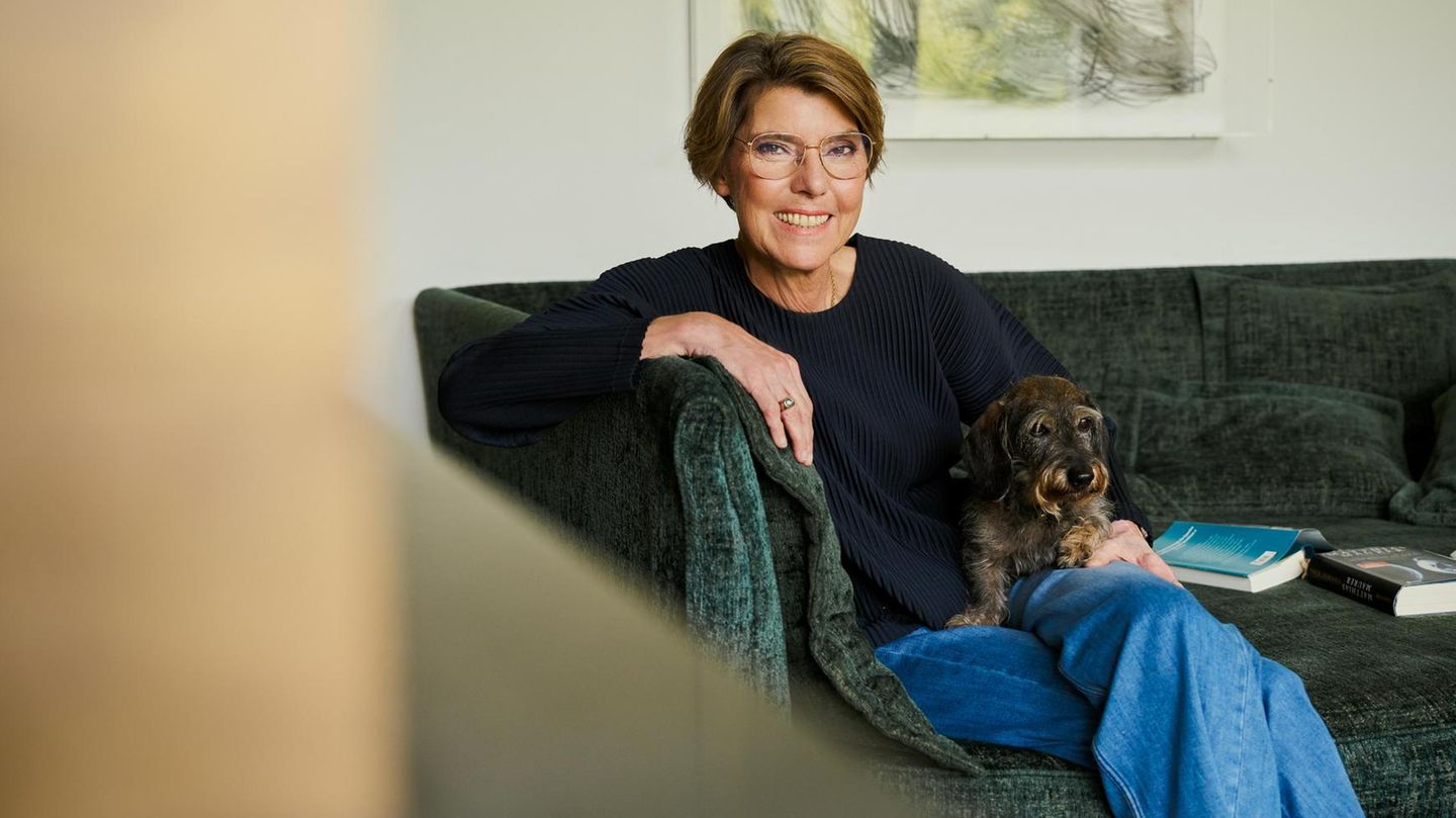 Bettina Böttinger sitzt auf einer Couch mit ihrem Dackel und lächelt in die Kamera