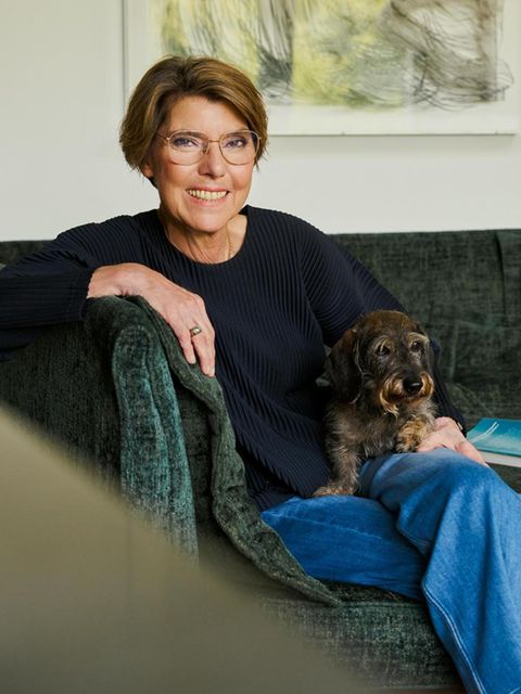 Bettina Böttinger sitzt auf einer Couch mit ihrem Dackel und lächelt in die Kamera
