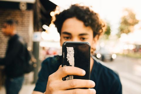 Junge mit Smartphone vor dem Gesicht: Bei der Erziehung von Jungs spielt es eine große Rolle