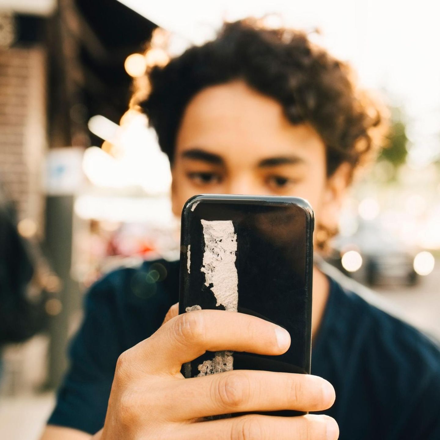 Junge mit Smartphone vor dem Gesicht: Bei der Erziehung von Jungs spielt es eine große Rolle