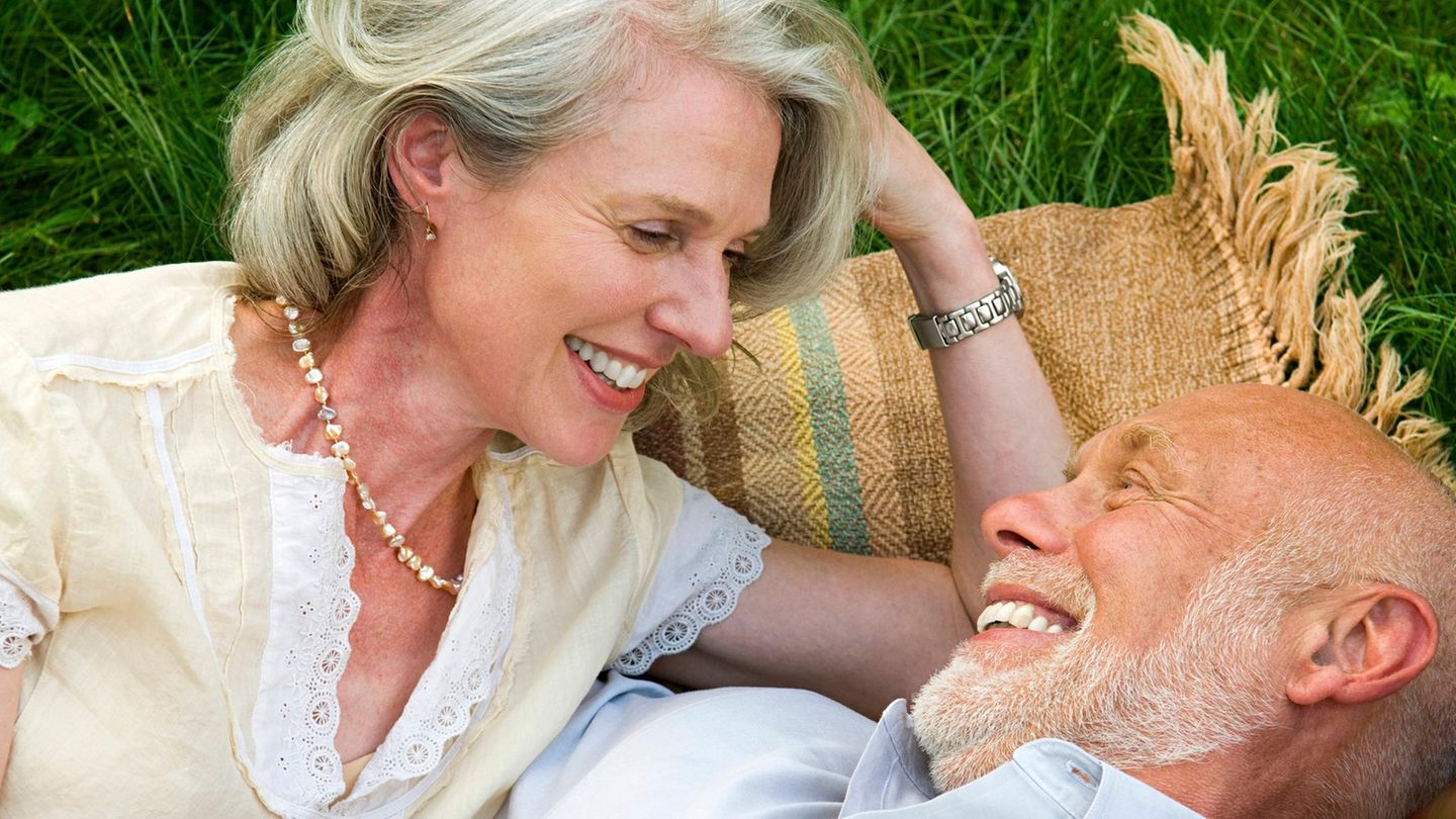 Älteres Paar liegt auf einer Picknickdecke und spricht über Rente