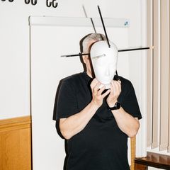 Fred Zack hält sich ein Kopfmodell mit Markierungen von Pfeilverletzungen vors Gesicht