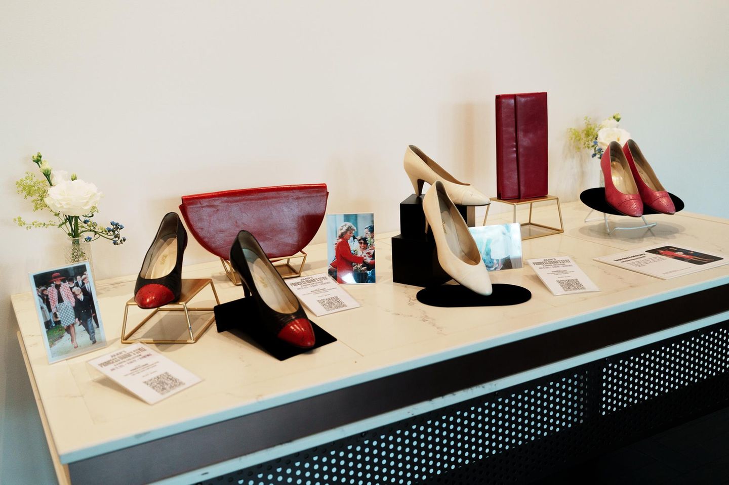 Ein Tisch mit drei Paar Schuhen, zwei Handtaschen, Fotos von Diana und Blumen
