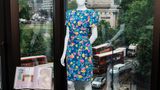 Eine Puppe trägt ein blumiges Kleid, dahinter zu sehen ist Londons Altstadt