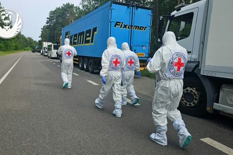 Arbeiter mit Rot-Kreuz-Abzeichen vor Kühl-Lkw mit Leichen