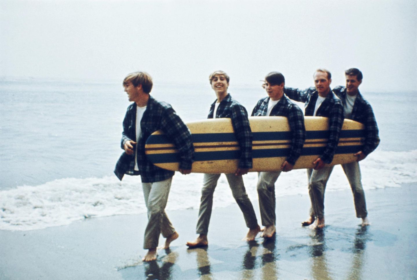 Brian Wilson und die Beach Boys mit Surfbrett unter dem Arm am Strand