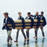 Brian Wilson und die Beach Boys mit Surfbrett unter dem Arm am Strand