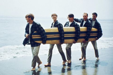 Brian Wilson und die Beach Boys mit Surfbrett unter dem Arm am Strand