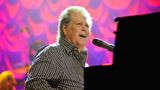 Brian Wilson sitzt am Klavier und singt in ein Mikrophon