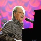 Brian Wilson sitzt am Klavier und singt in ein Mikrophon