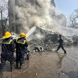 Mitglieder des Rettungsteams löschen, während Rauch an der Absturzstelle in Ahmedabad aufsteigt