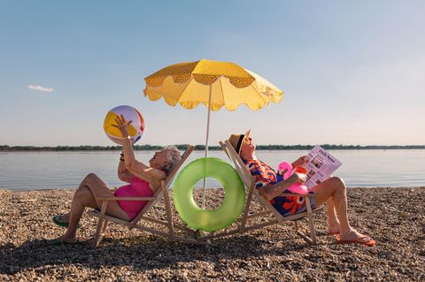 Porträt von Rentnern, die auf einer Strandliege unter einem Sonnenschirm sitzen.