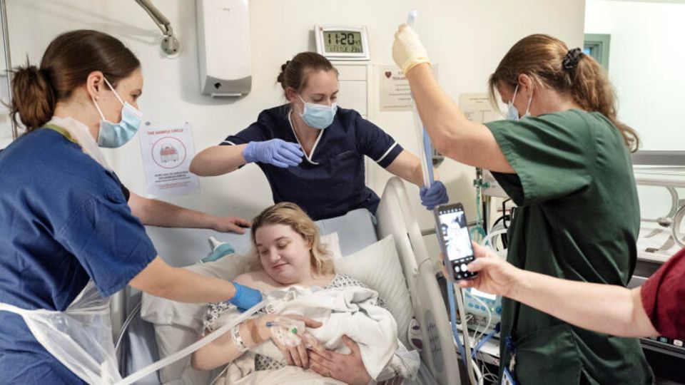 Mutter mit Baby im Krankenbett und drumherum Krankenschwestern