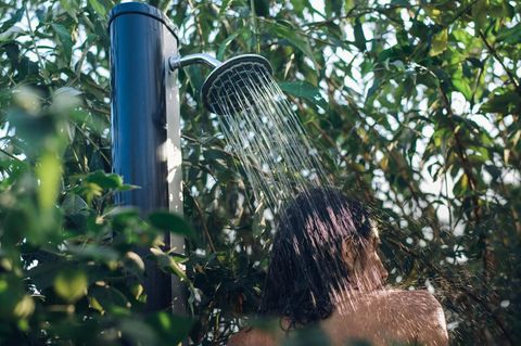 Eine Frau duscht unter ihrer Solardusche im Garten