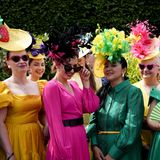 EInen gruppe von Frauen in bunten Kleidern und farbenfrohen Hüten mit Federn beim Royal Ascot