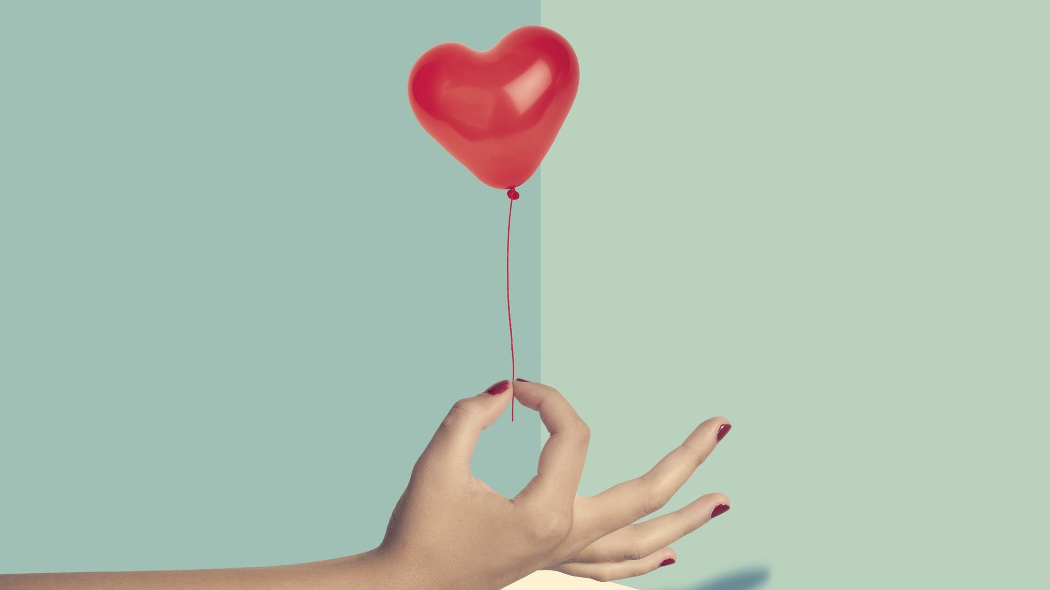 Eine Hand hält einen kleinen Herz-Luftballon