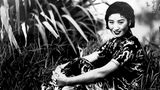 Eine Frau in einem chinesischen Kleid sitzt lächelnd im Gras, die Arme anmutig um die Beine geschlungen, schwarz-weiß, um 1940