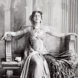 Frau im exotischen Schleiertanzgewand, das viel Haut zeigt, auf einer Art antikem Thron sitzend; SW-Foto, um 1906