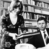 Eine schlanke Frau mit Akten in beiden Händen neben einem kurzhaarigen Mann an einem Schreibtisch, schwarz-weiß, 1970er Jahre