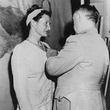 Ein Mann steckt einer Frau in Kleid und mit hellem Haarband einen Orden an, schwarz-weiß, 1945