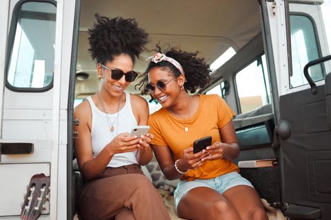 Zwei Frauen sitzen lachend mit Smartphones in einem Camper.