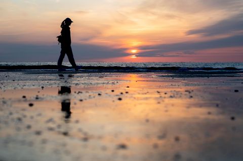 Eine junge Frau spaziert bei Sonnenuntergang am Strand entlang